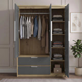 [Grey] wardrobe with grey doors and drawers, shown open and styled with clothes and folded garments inside. The wardrobe is set against a paneled beige wall with a potted plant on the right.