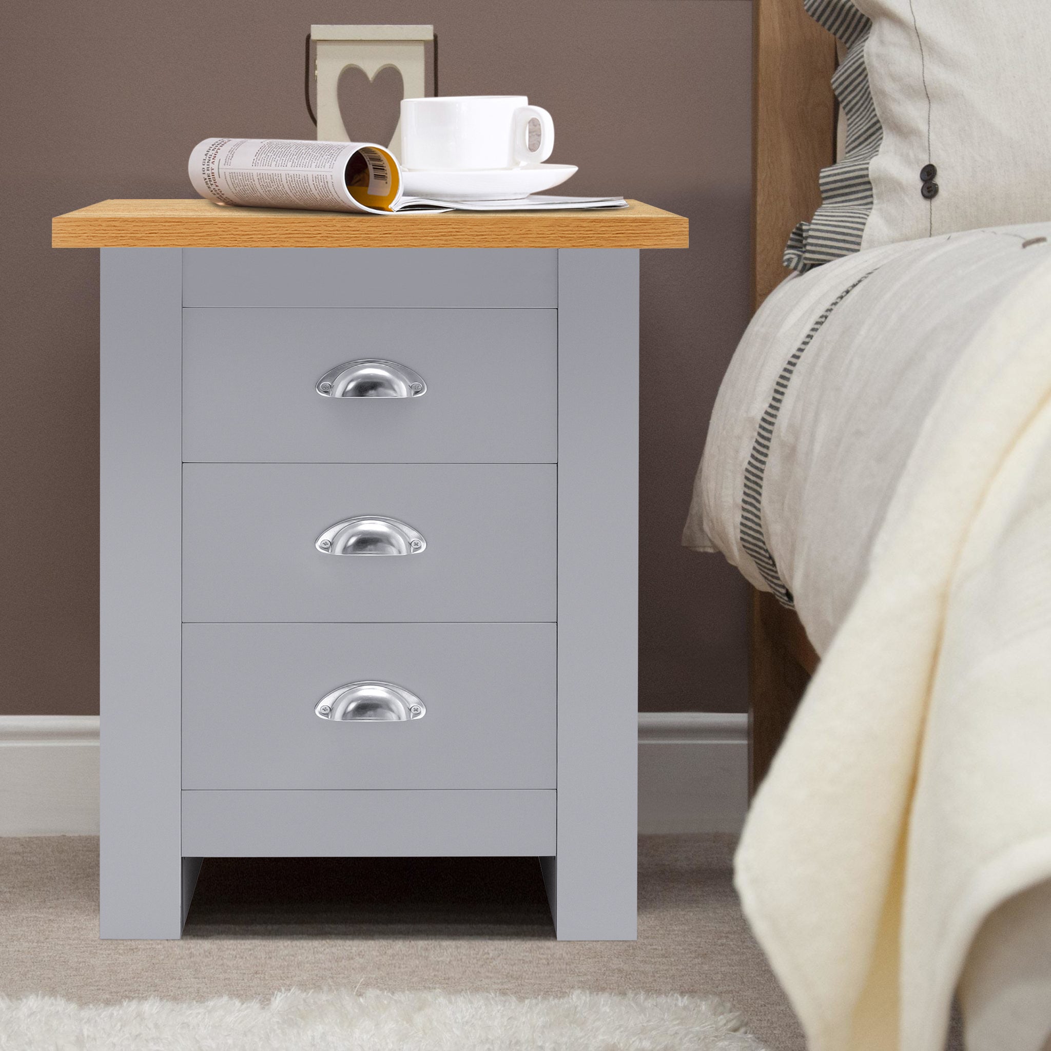 Grey 3-drawer bedside table with silver handles, oak top, cup, and magazine placed on top