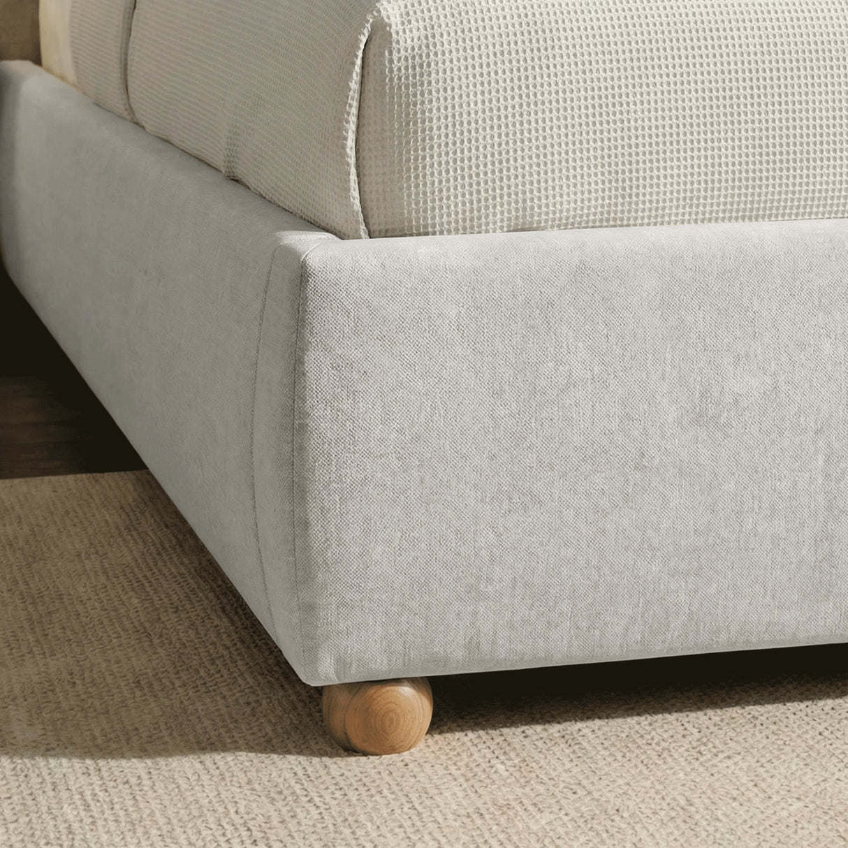 Close-up detail of the bottom base of the grey king upholstered bed frame with rounded wooden feet