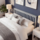Wooden grey bed frame with a headboard having a slatted pattern, with layered pillows and bedside furniture in bedroom
