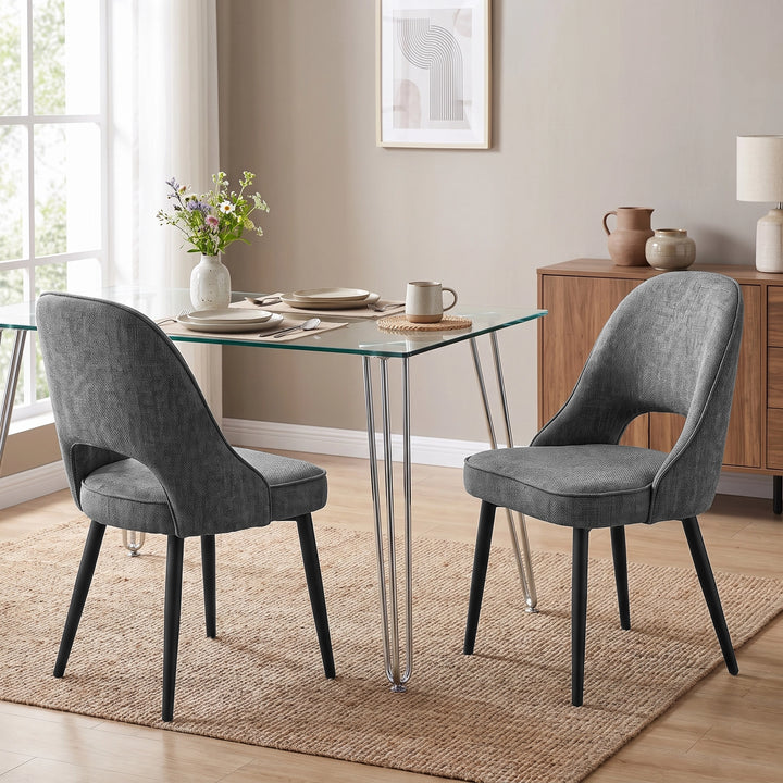 [Grey | Set of 4] Pair of fabric dining room chairs at a glass table, showing curved open backs and black metal legs