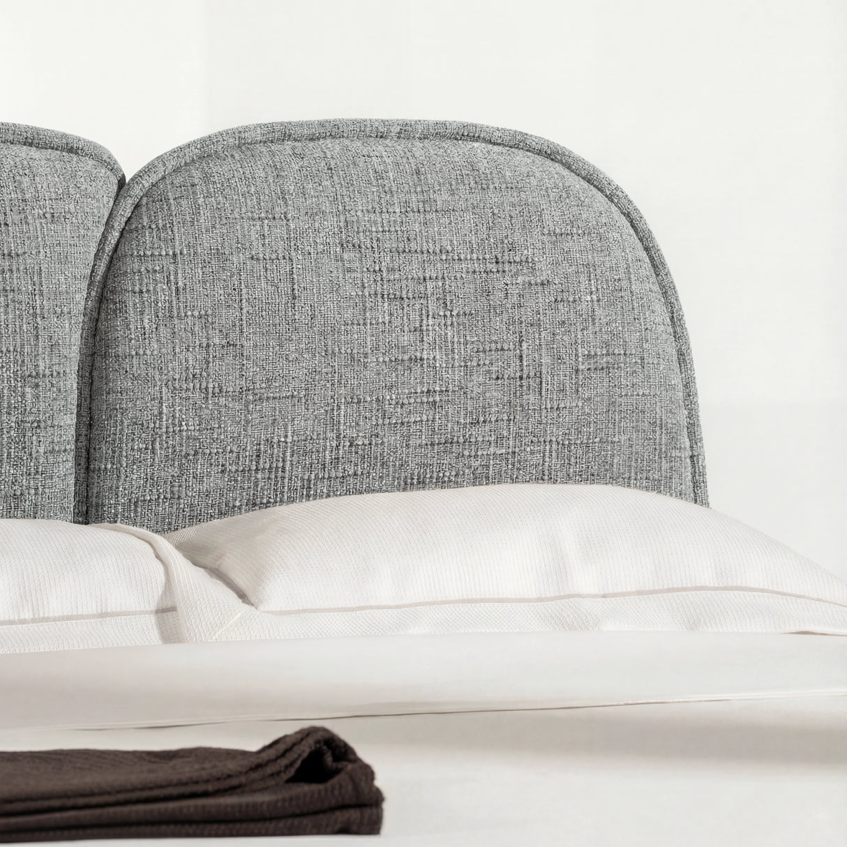 Close view of a curved padded backrest with textured fabric, placed above smooth neutral bedding