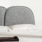 Close view of a curved padded backrest with textured fabric, placed above smooth neutral bedding