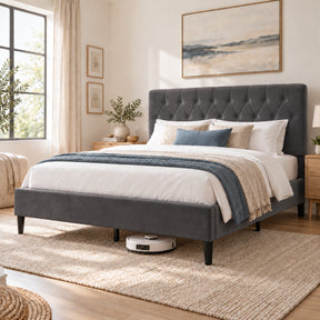 [Double | Grey] Angled bedroom view showing a robot vacuum beneath the bed frame, tufted headboard, bedding, and woven rug.