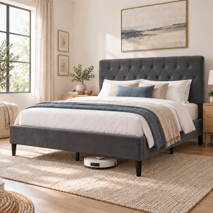 [Double | Grey] Angled bedroom view showing a robot vacuum beneath the bed frame, tufted headboard, bedding, and woven rug.