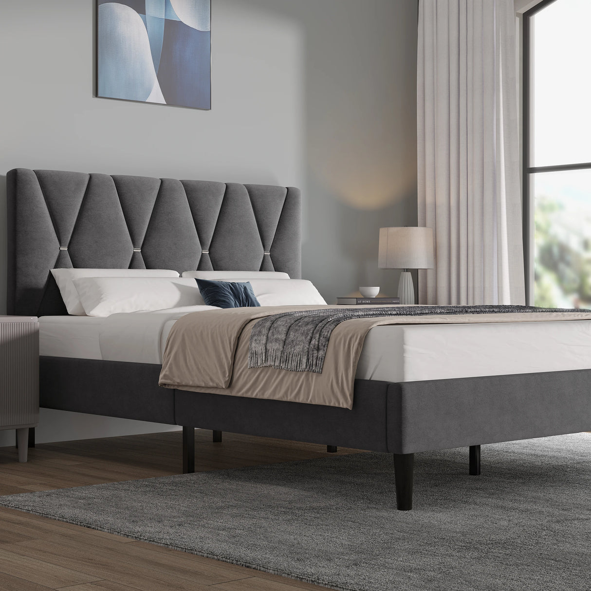 Gray upholstered bed in a modern bedroom with a lamp and abstract painting.