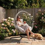 [Grey] Woman relaxing in a hanging chair with a dog in a garden setting
