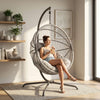 [Grey] Woman sitting in a hanging egg chair in a bright room with plants and shelves