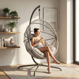 [Grey] Woman sitting in a hanging egg chair in a bright room with plants and shelves
