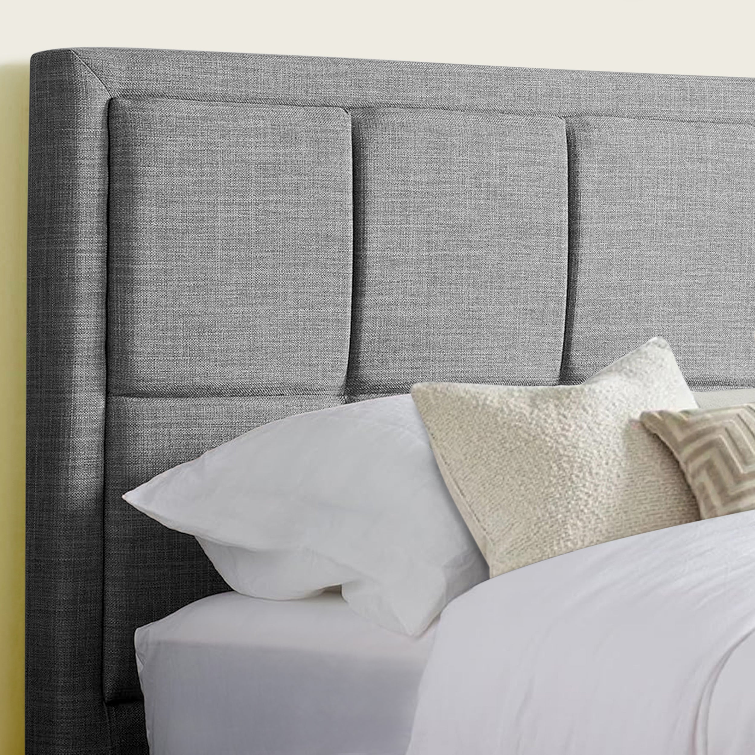 Close-up of a grey fabric upholstered headboard with soft pillows and bedding.