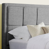 Close-up of a grey fabric upholstered headboard with soft pillows and bedding.