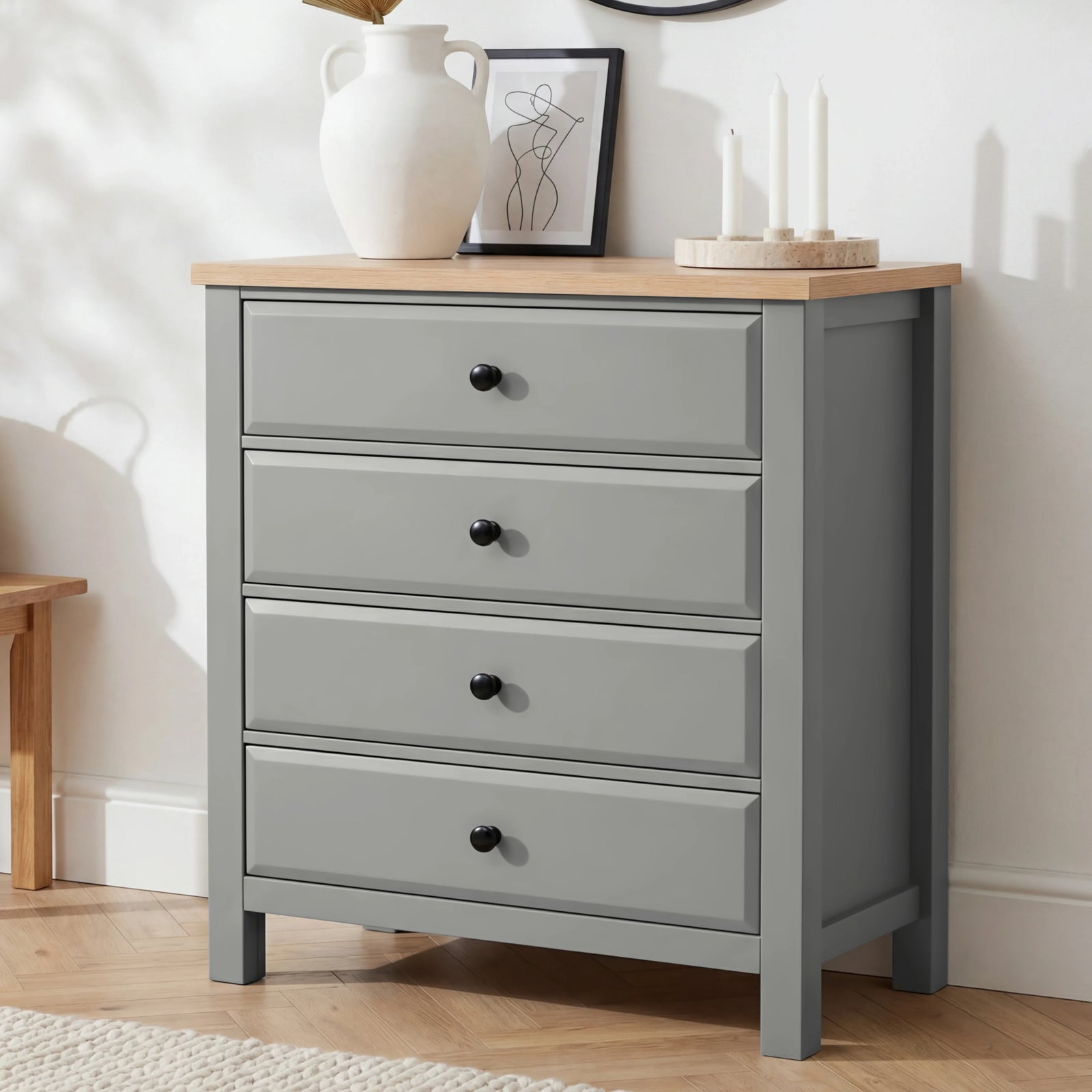 [Grey] Haven 4 drawer chest with oak top and black knobs at a three-quarter angle, styled with dried botanicals and candles