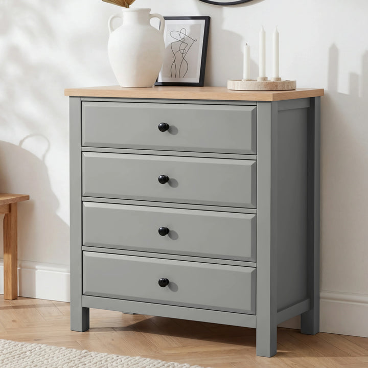 [Grey] Haven 4 drawer chest with oak top and black knobs at a three-quarter angle, styled with dried botanicals and candles