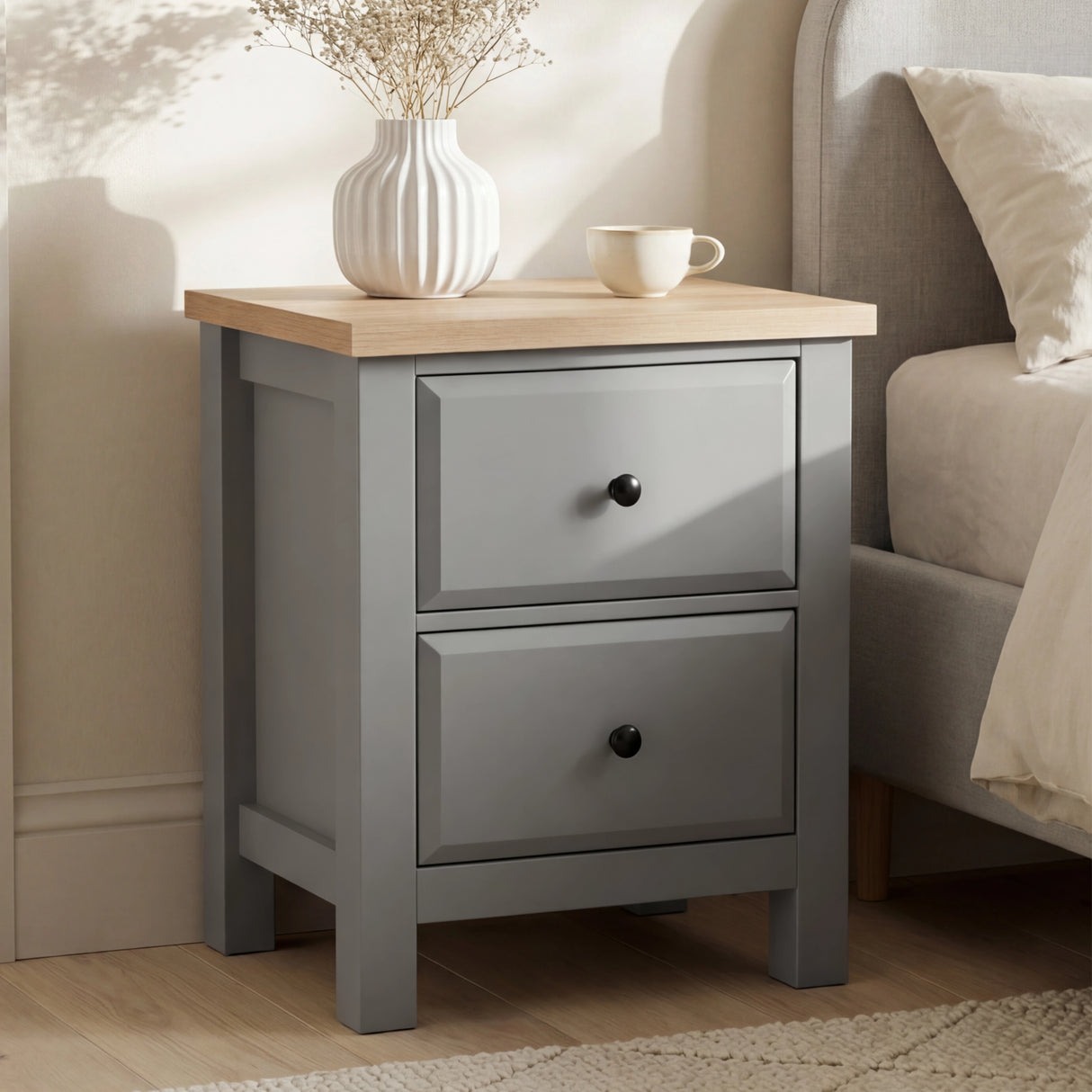 [Grey] Haven bedside table styled beside a linen upholstered bed with dried flowers and mug on oak top