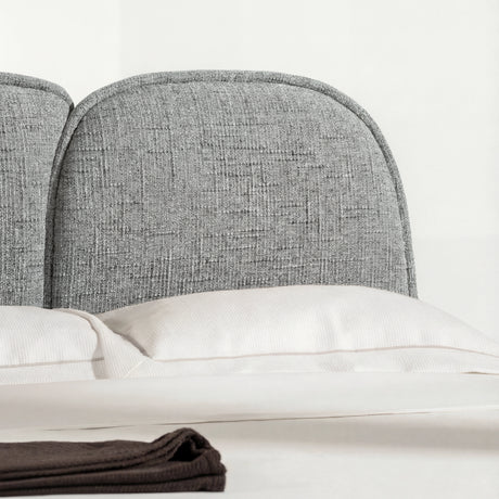 Close view of a grey upholstered bed backrest with curved edges, and neutral bedding arranged