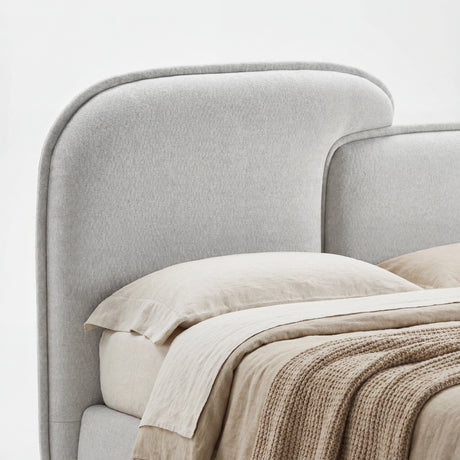 Close view of a softly curved, split-style padded headboard in grey fabric with subtle fabric texture