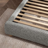 Angled detail of a fabric-wrapped bed perimeter with exposed wooden slats forming the internal mattress support structure
