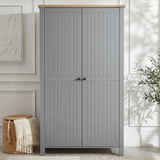[Grey] Linra 2 Door Wardrobe front view in a white panelled room with woven basket and throw beside it and olive tree to the right