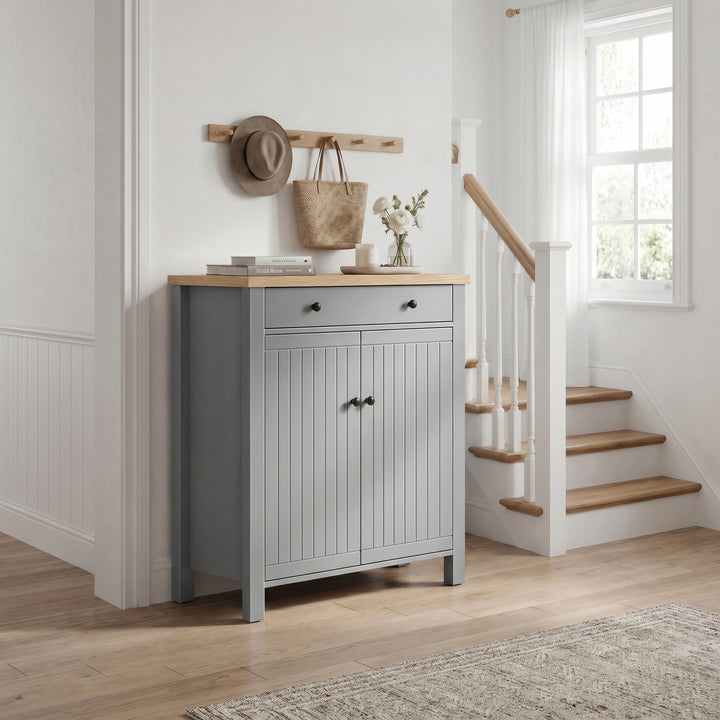 [Grey] Linra Grey 4 Tier Painted Shoe Storage Cabinet With Drawer three-quarter view in styled hallway with staircase, coat hooks and flowers on oak top