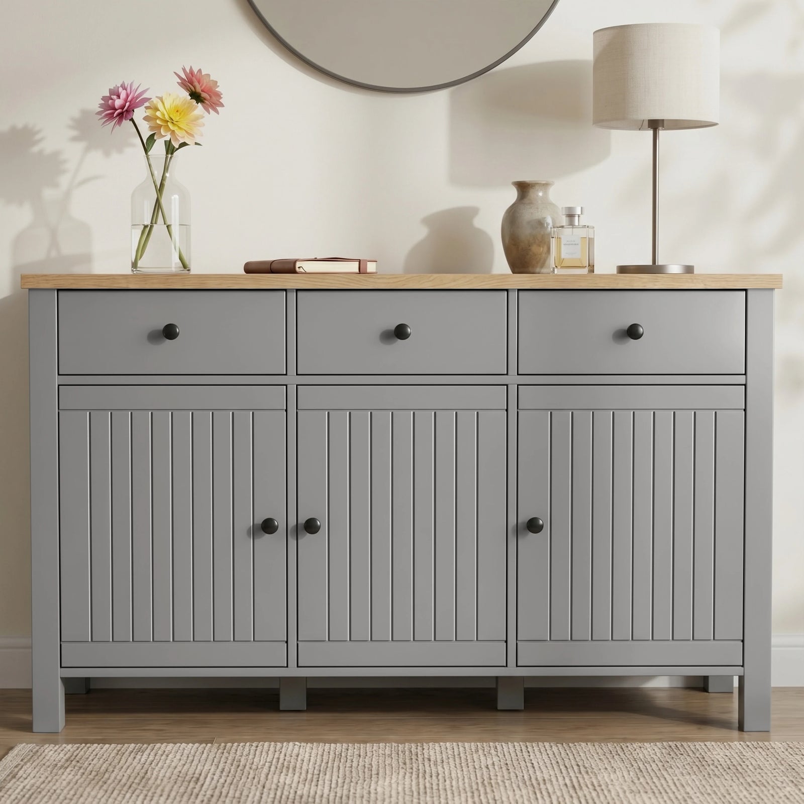 [Grey] Linra straight front detail showing three drawers, beadboard doors, oak-effect top, lamp, and vases