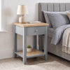 [Grey] Angled view of Grey Shaker Bedside Table with natural oak top, drawer, and open shelf styled by bed.