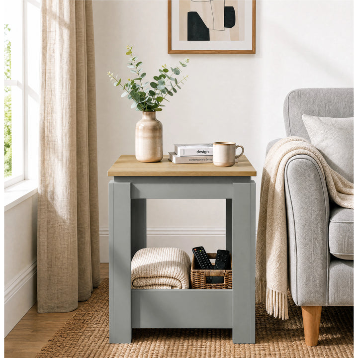 [Grey] Front view of the square side table beside a sofa, with a folded throw and basket stored below