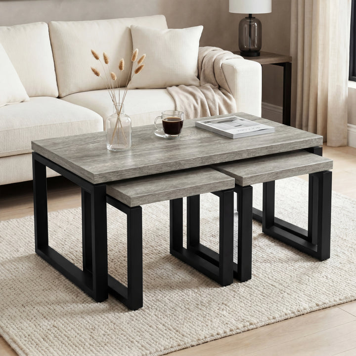 [Grey Oak] Nestline table set beside a cream sofa, with soft cushions, flowers, and black nesting frames