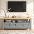 [Grey] Oskara TV unit front view in living room below wall-mounted TV styled with blossom vase, white ribbed vase, gold candles, and table lamp