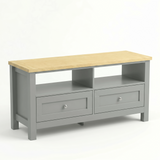 [Grey] Oskara TV unit isolated three-quarter view on white background showing oak top, two open shelf bays, and two shaker drawers with metallic knobs