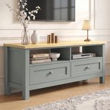 [Grey] Oskara TV unit angled view in living room below a TV with two open shelves, shaker drawers, blossom vase, gold candles, and bedside lamp