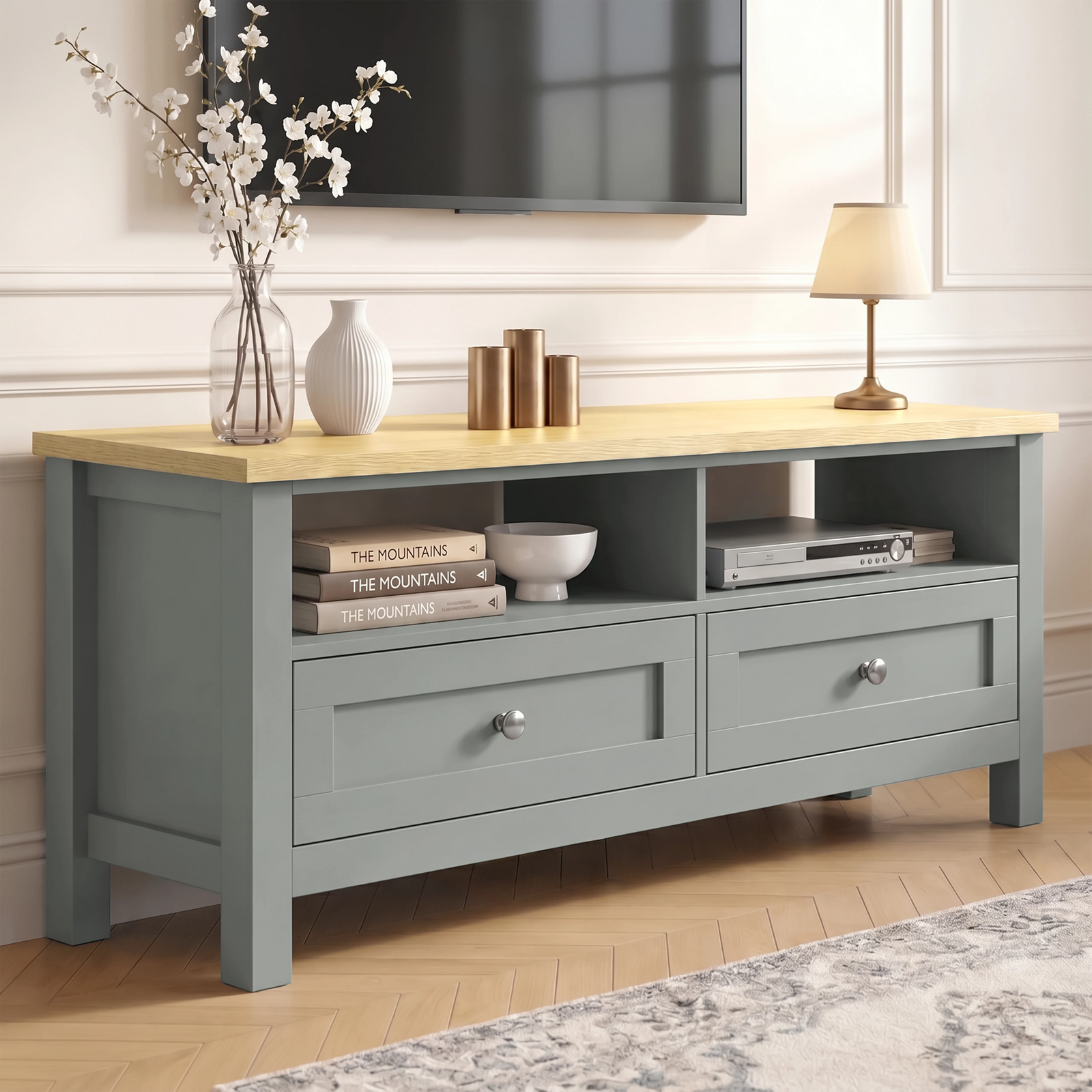 [Grey] Oskara TV unit angled view in living room below a TV with two open shelves, shaker drawers, blossom vase, gold candles, and bedside lamp