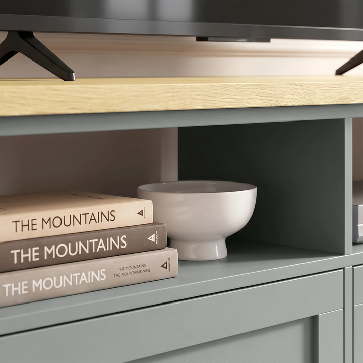 [Grey] Oskara TV unit close-up of open shelf cubby holding stacked books and a white ceramic bowl below a stand-mounted TV on oak top
