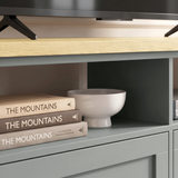 [Grey] Oskara TV unit close-up of open shelf cubby holding stacked books and a white ceramic bowl below a stand-mounted TV on oak top