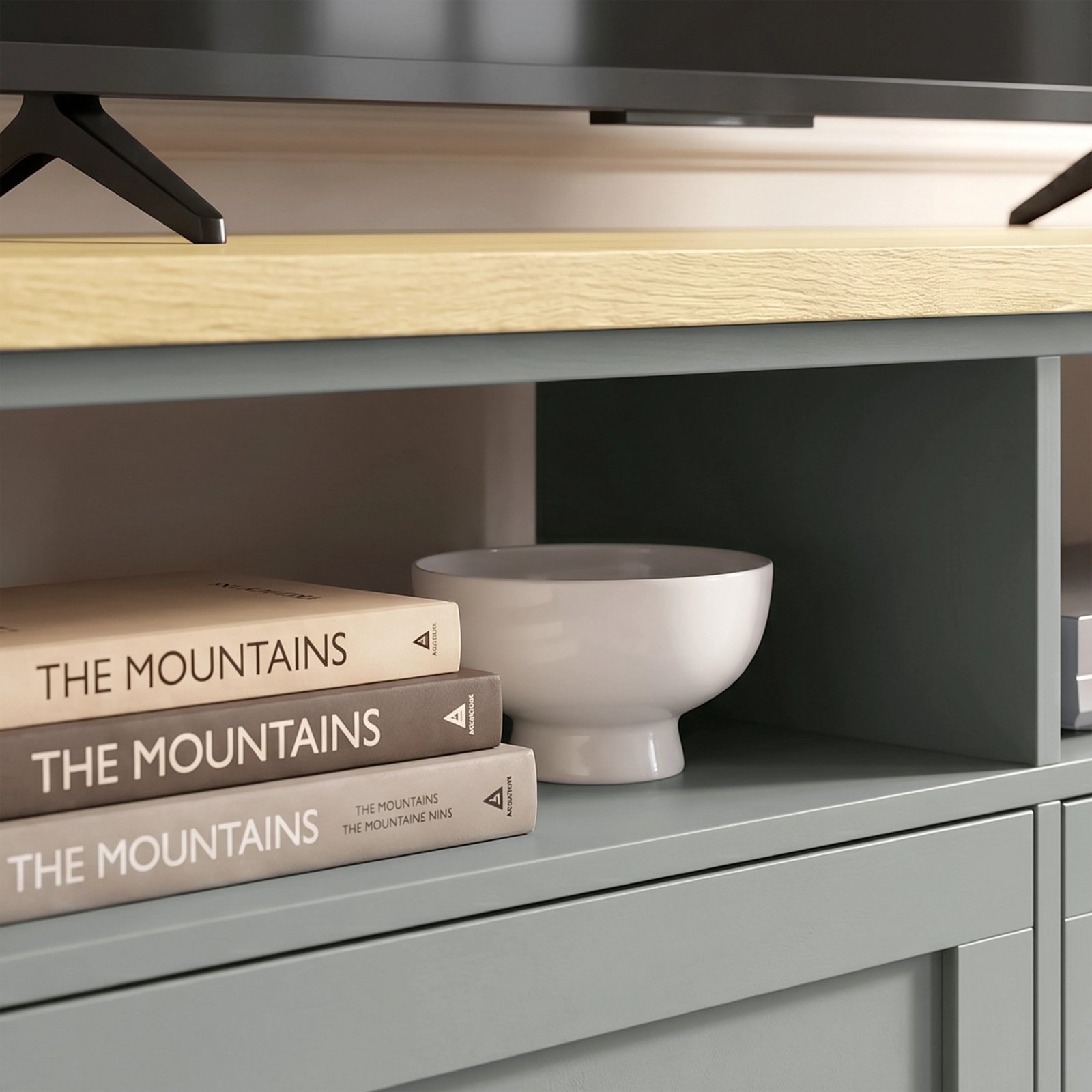 [Grey] Oskara TV unit close-up of open shelf cubby holding stacked books and a white ceramic bowl below a stand-mounted TV on oak top