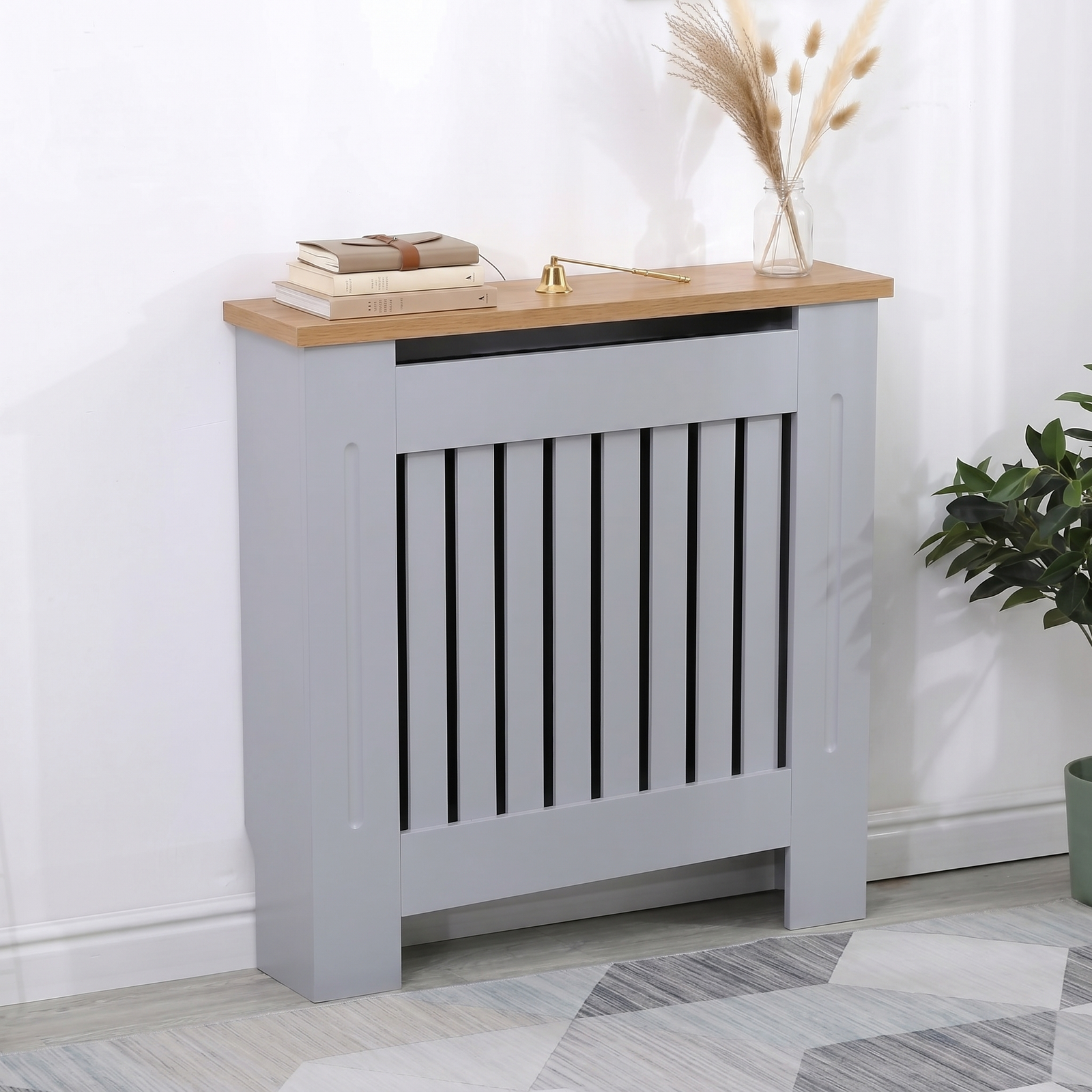 [Small | Grey] Radiator Cover with oak top shelf displayed at an angle styled with books, a brass ornament, and a pampas vase beside a potted plant