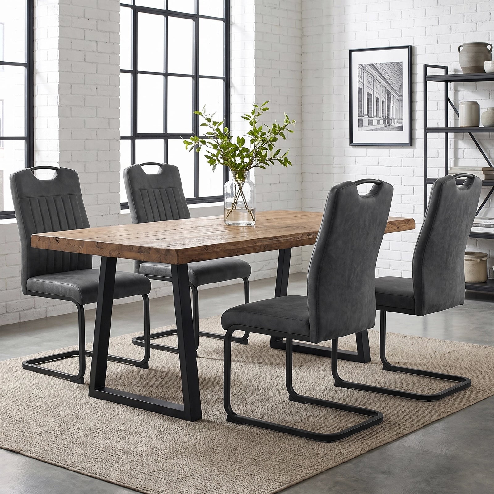 [Grey] Four high-back dining chairs with black loop frames around a wood table styled with a glass plant vase.