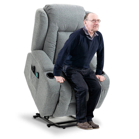 Elderly man using grey riser recliner chair in lift mode. Provides support and ease of standing for elderly users.