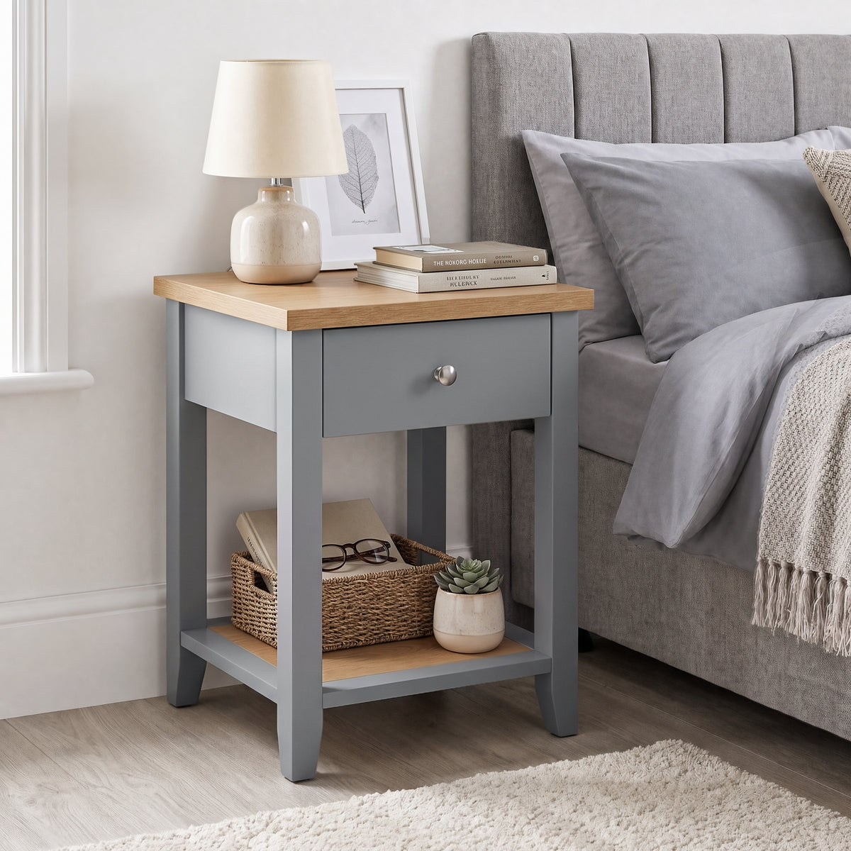 [Grey] Angled view of Grey Shaker Bedside Table with natural oak top, drawer, and open shelf styled by bed.
