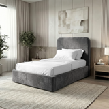 Angled view of grey velvet single ottoman storage bed highlighting padded headboard and soft finish frame
