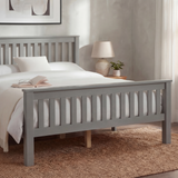 Grey wooden double bed frame with slatted rail pattern and layered bedding, placed in a natural light room
