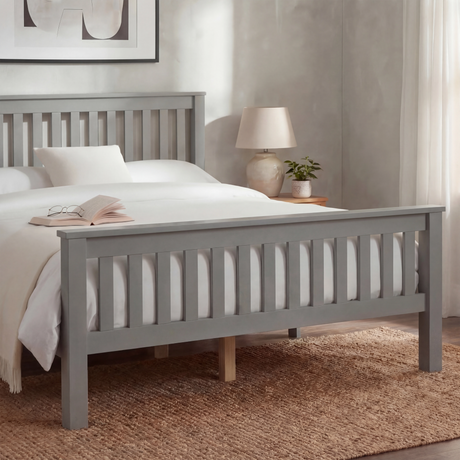 Grey wooden double bed frame with slatted rail pattern and layered bedding, placed in a natural light room