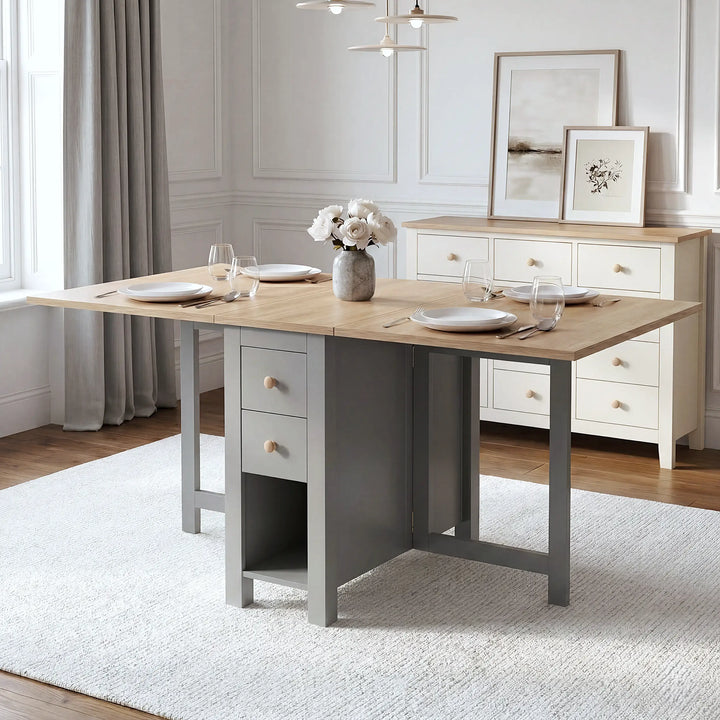 [Grey] Stovra Drop Leaf Dining Table fully extended with both leaves up, set for four with place settings, glasses, and a rose flower centrepiece