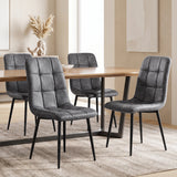[Grey] Four suede dining chairs around a rectangular wood-effect table, showing tufted fronts and rear profiles.