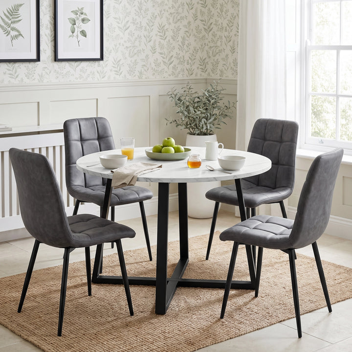 [Grey] Four suede dining chairs with tufted seats, curved backs and slim legs around a round white table.