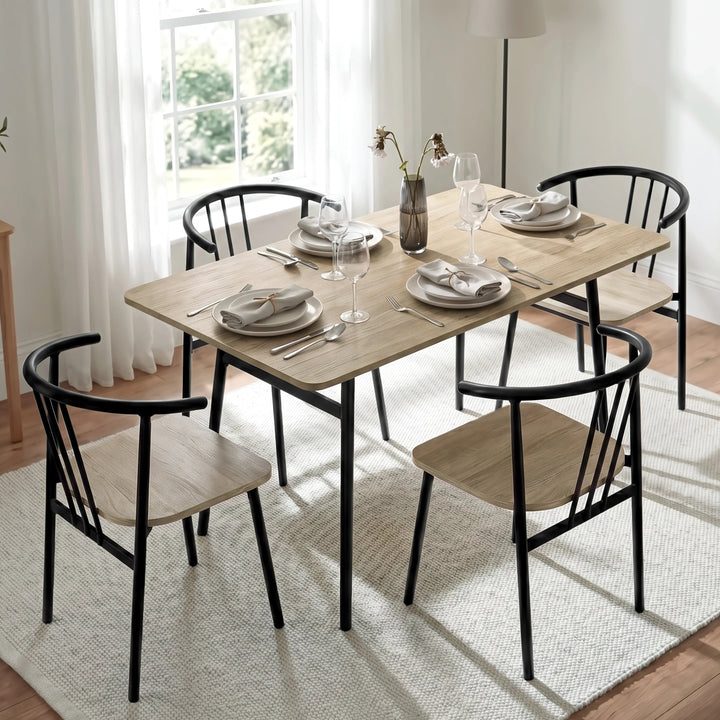 [Grey] Torvi dining scene showing four spindle-back chairs, plates, folded napkins, wine glasses, vase, and floor lamp.