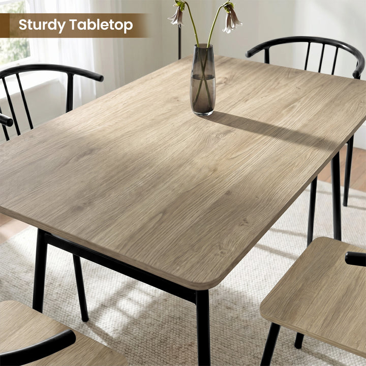 [Grey] Torvi tabletop close-up showing wood-grain pattern, rounded corner, slim metal legs, curved chair backs, and vase.