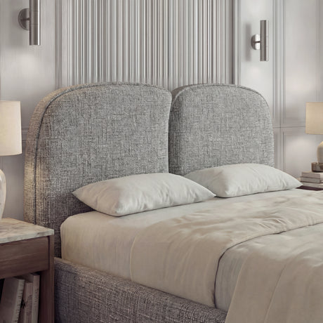 Close detail of a textured fabric backrest bed frame with softly curved edges positioned above neatly layered bedding