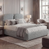 King-size grey upholstered bed frame with curved back panels, layered textiles, placed in a natural light bedroom
