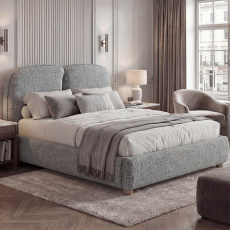King-size grey upholstered bed frame with curved back panels, layered textiles, placed in a natural light bedroom