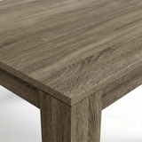 [Wooden Grey] Close-up of the grey wood-effect tabletop corner and thick L-shaped leg; mixed grain runs across both surfaces.